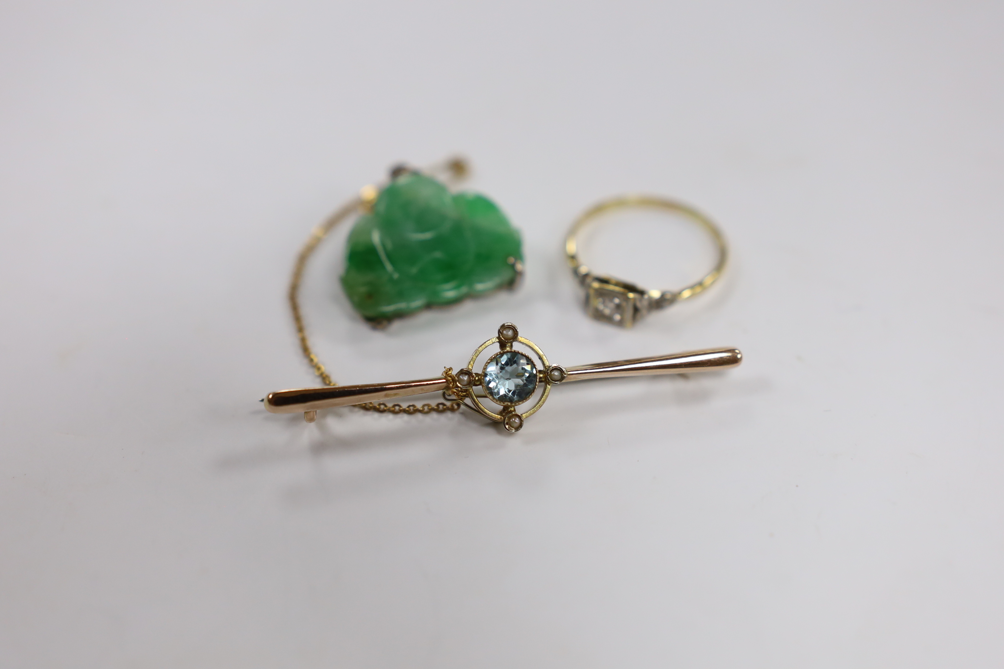 An Edwardian 9ct, aquamarine and seed pearl cluster set bar brooch, 54mm, a Chinese mounted jade Buddha pendant and an 18ct and single stone diamond set ring, with diamond chip set shoulders.